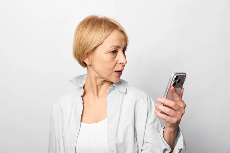 Elderly woman, smartphone in hand, focused expression, communication and technology concept, she checks messages, indoor studio on white background, senior lifestyle