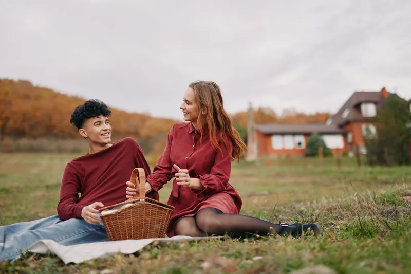 Young couple enjoying a genuine outdoor picnic in a rural meadow, sharing smiles and simple moments, natural clothing and relaxed posture conveying authenticity and credibility.