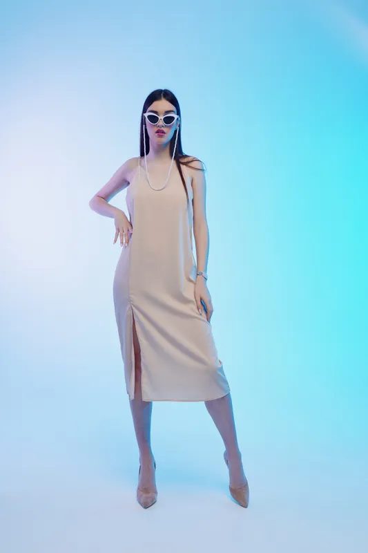 Woman beauty fashion model poses in beige dress with sunglasses and pearls on blue gradient background. Studio shot with stylish and elegant concept.