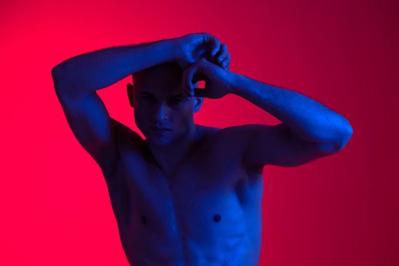 Athletic man posing in dynamic light, showcasing strength and emotion. The vibrant color contrast emphasizes his physicality and artistic expression.