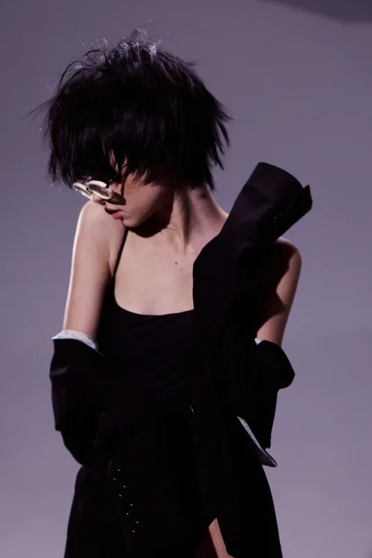 Stylish woman with short hair wearing sunglasses and black outfit posing against gray background