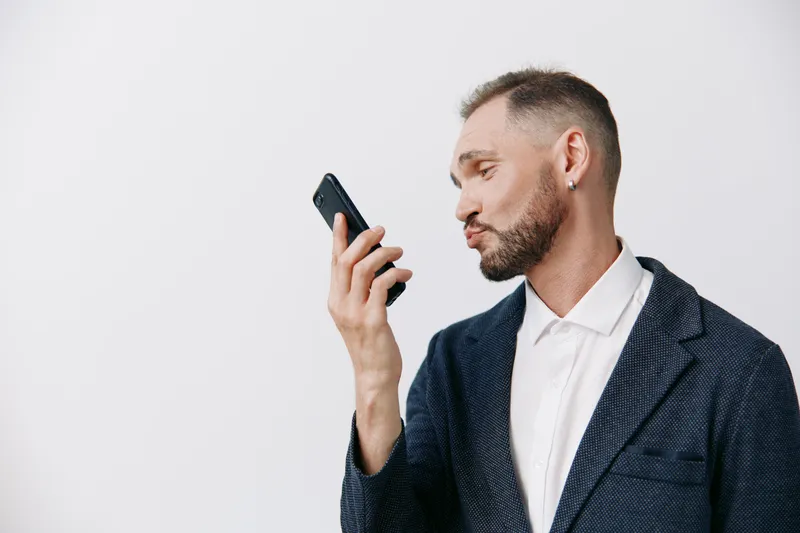 A businessman in a tailored suit interacts with a smartphone against an isolated colored background, showcasing confidence, focus, and professional poise.