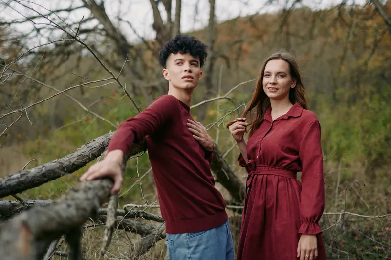 Candid outdoor portrait of a young couple on a fallen tree, showing authentic connection and credible emotion through relaxed poses, natural expressions, and sincere body language.