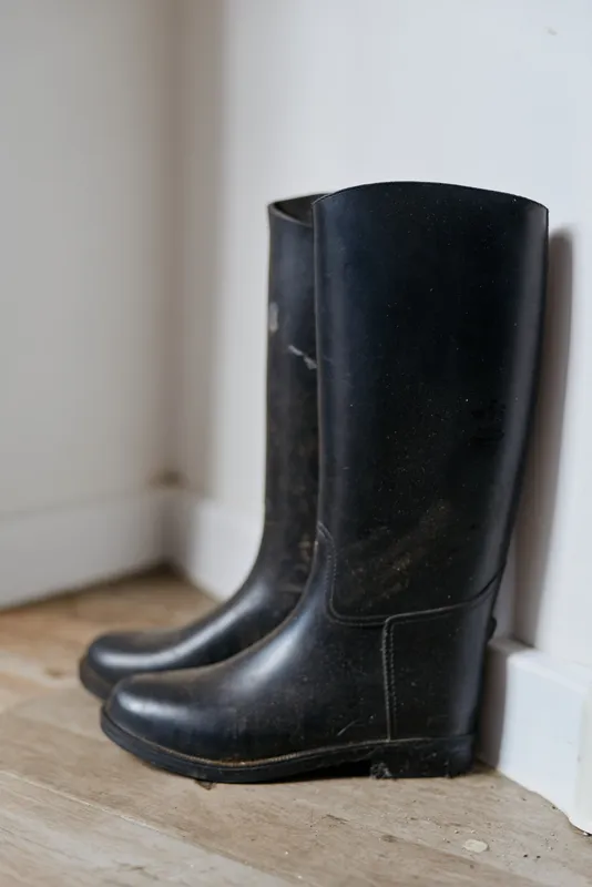 Black leather boots rest by a light interior wall, a minimalist home scene with modern style and calm mood, showing everyday footwear in a simple urban setting