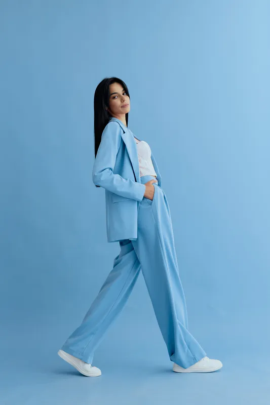 young woman walking confidently in blue suit with white sneakers on a plain blue background, stylish casual outfit, modern fashion look