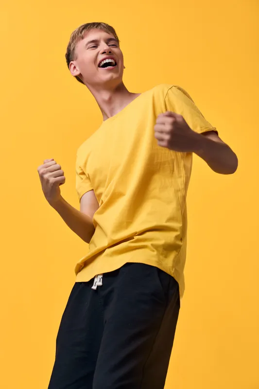 Joyful man wearing a yellow tshirt dances against a bright yellow background, capturing energy and happiness in a casual studio scene, emphasizing motion and vibrant mood for lifestyle and fashion