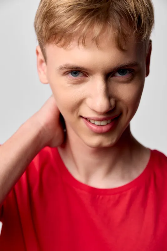 Smiling young man in a bright red shirt poses in a clean studio, conveying confidence and friendliness for lifestyle, fashion, or marketing visuals. The image highlights approachability.