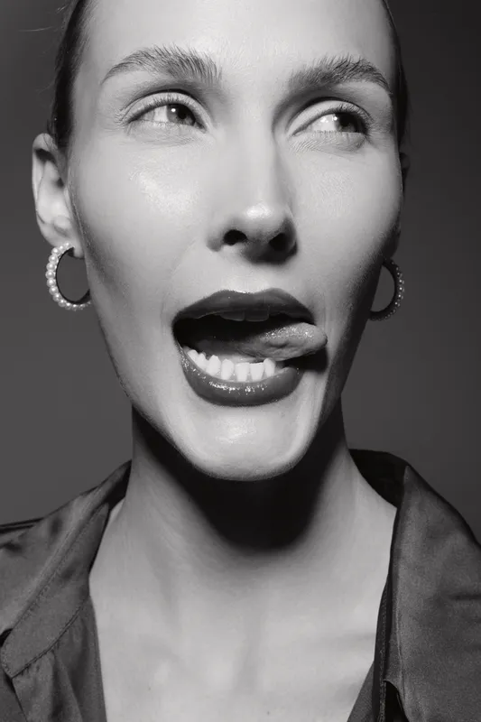 Close-up black and white portrait of a fair skinned Caucasian woman with earrings, licking lips and looking to the side. Concept for beauty, expression, and fashion.