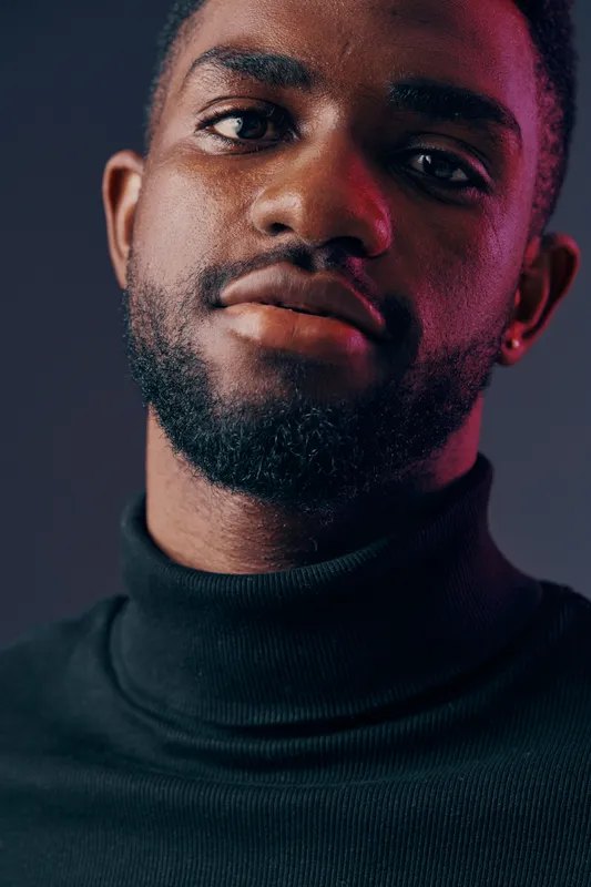 Close up portrait of a confident Black man in a turtleneck, conveying determination and style against a dark background with vibrant lighting
