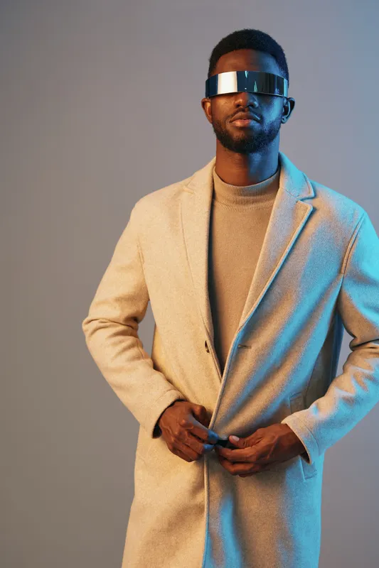 Stylish male model in a modern coat with futuristic sunglasses, showcasing urban fashion trends against a gradient background, perfect for contemporary lifestyle branding
