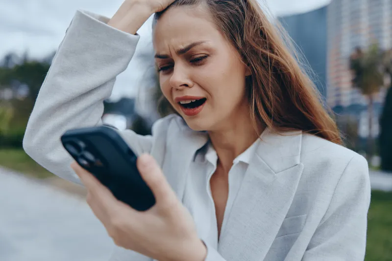 upset woman in business suit holding smartphone outdoors stressed by financial crisis and stock market drop