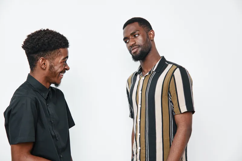 Two African American men with dark skin smiling and talking together in casual clothing on white background. Friendship, communication and positive interaction.