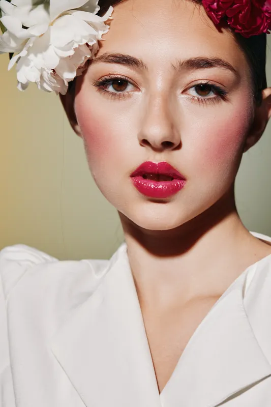 Close-up portrait of a young woman with bright red lipstick and floral headpiece. Glamorous beauty and fashion concept with soft lighting highlighting vivid makeup details.