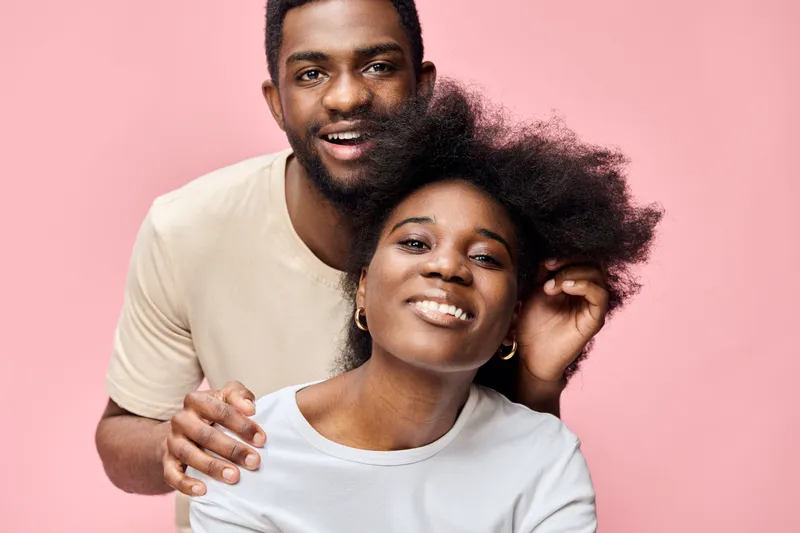 Happy African American couple with natural hair, smiling against a pink background, representing love, joy, and connection in a vibrant, modern style