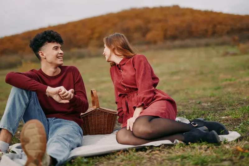 Authenticity and credibility frame a candid moment as two figures sit on a blanket in an autumn meadow, sharing warm conversation beside a wicker picnic basket.