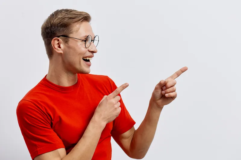 Smiling man wearing red t-shirt and glasses point fingers side isolated on white background casual style digital nomad concept