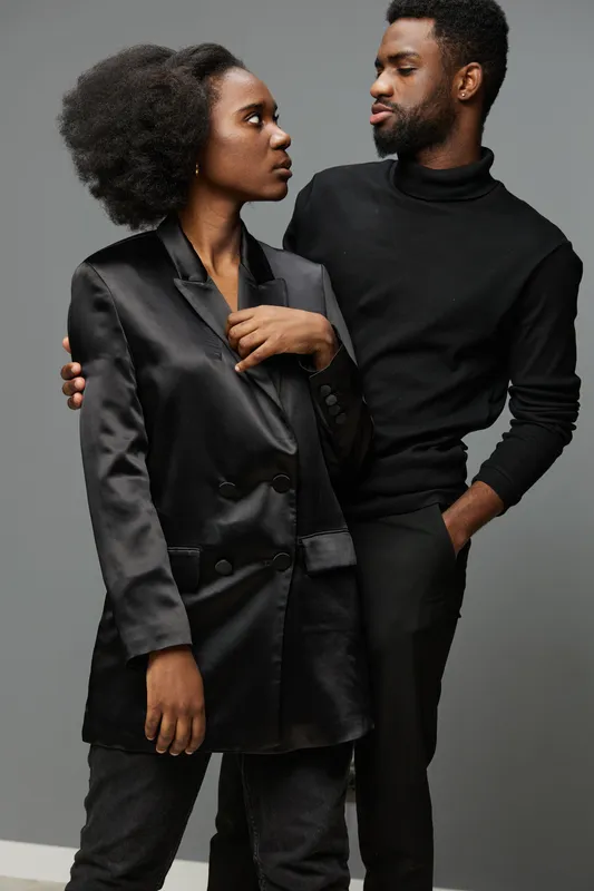 Stylish black couple in modern attire, showcasing confidence and emotion with a neutral gray background, portraying contemporary fashion and elegance