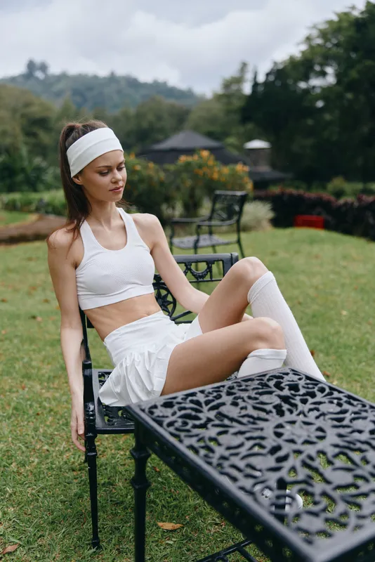 Young fitness woman in sporty outfit resting on a garden chair, showcasing athletic wear in a serene outdoor setting, perfect for wellness concepts