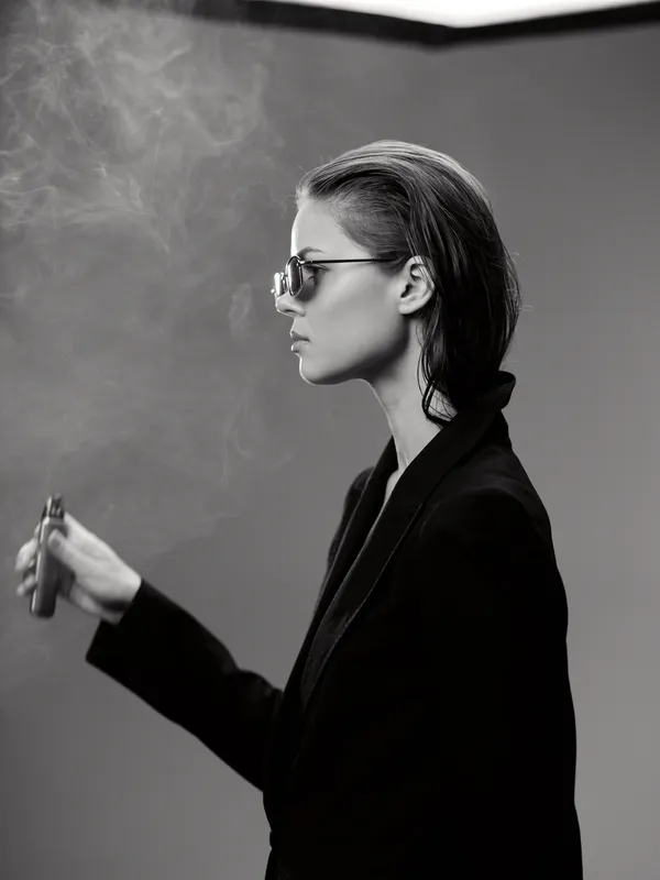 Black and white portrait of a stylish woman wearing sunglasses smoking with smoke around her.