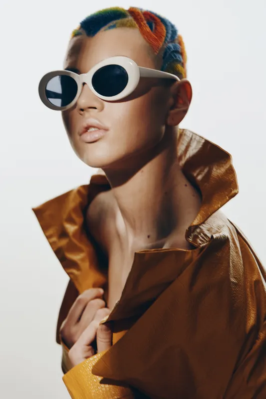 woman with colorful hair and white sunglasses wearing a brown textured jacket, vibrant fashion look, artistic lighting, modern style portrait