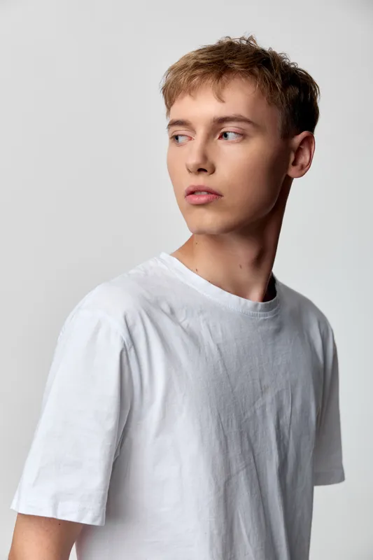 Young man wearing a white t shirt with a thoughtful gaze, casual wear in a studio setting, clean background, minimal styling, ideal for fashion lifestyle stock imagery
