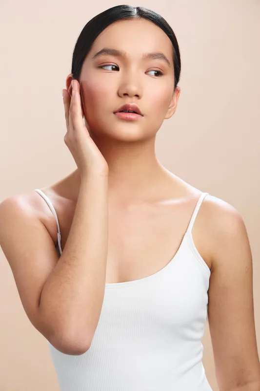 Asian woman in a clean studio portrait poses with her hand resting beside her face, showcasing calm elegance, subtle makeup, refined features, and contemporary beauty.