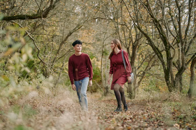Authentic moment as a couple walks through a quiet autumn forest, casual outfits, natural light, candid interaction, sincere connection, unposed mood, subtle motion.