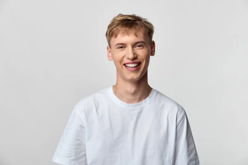Smiling young man in a white tee, studio setting with casual mood, front view and bright background, cheerful expression ideal for lifestyle advertising and stock use