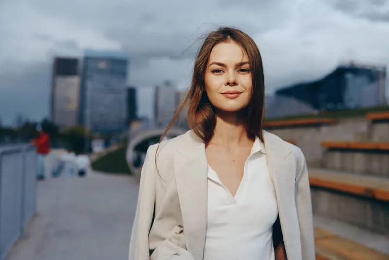 confident woman in business casual wear smiling outdoors with city buildings in background in urban fashion style