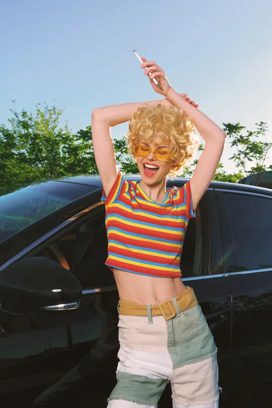 Woman lifestyle retro colorful sunny fashion cheerful summer pose beside a car, capturing bold retro vibe with rainbow stripes, bright mood, and carefree energy.