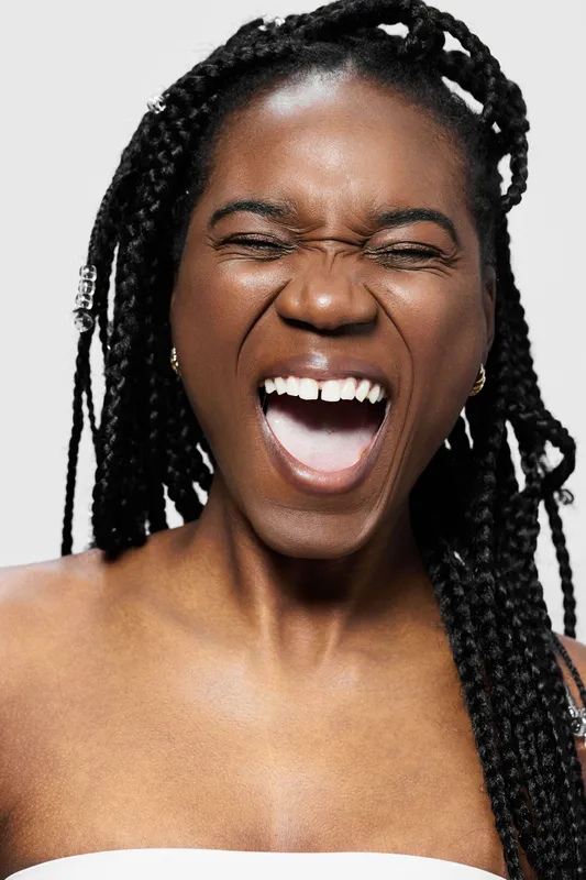 Happy black woman with braids joyfully laughing against a light background, embodying positivity and self confidence in a bright and vibrant setting