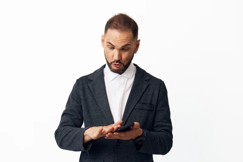 Professional businessman shown in a focused pose while using a mobile device. The isolated colored background highlights his confident, calm presence and strong work ethic.