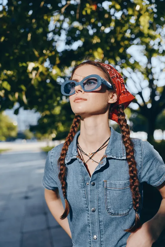 Lifestyle woman in modern boho-western denim street style wearing oversized blue sunglasses and red bandana, captured with film color for a trendy urban look.