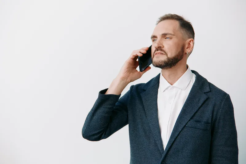 Portrait of a business professional man on a solid colored background, speaking on a mobile phone, conveying focus, confidence, and calm leadership.
