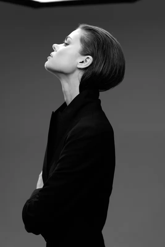 Black and white portrait of a woman in a black coat with elegant hairstyle and serene expression.
