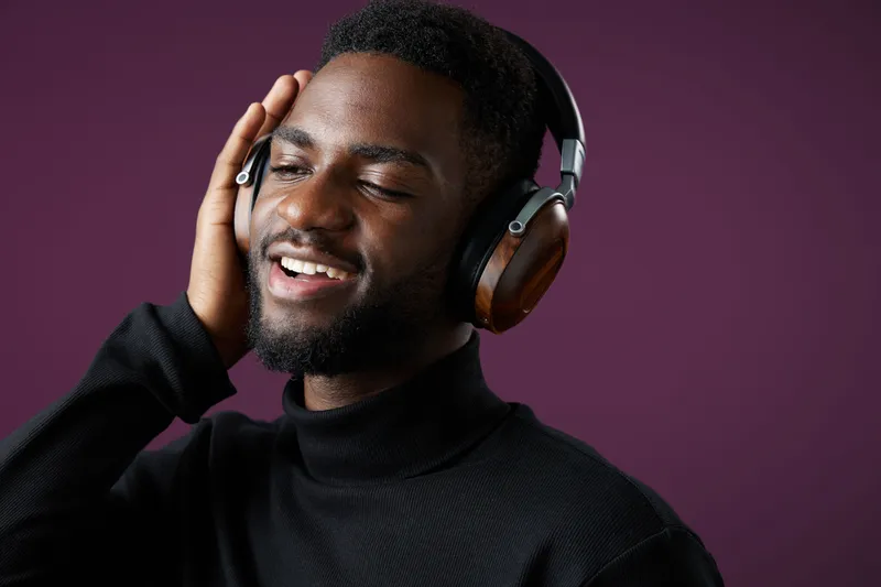 Young Black man enjoying music with headphones on a purple background, expressing joy and relaxation in a trendy outfit