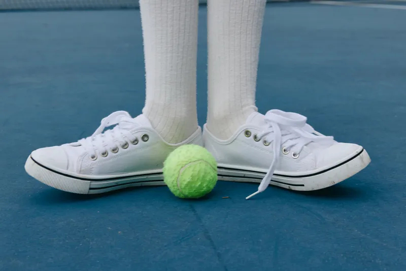 White sneakers on a tennis court with a green tennis ball, emphasizing sports footwear and active lifestyle in a vibrant, energetic setting