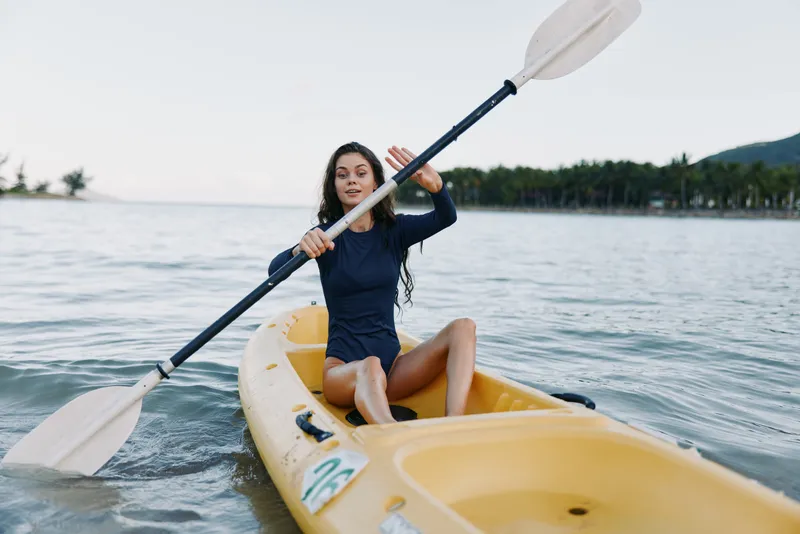 young woman kayaking on calm lake wearing dark swimsuit with paddle in hand enjoying outdoor activity under clear sky