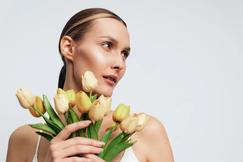 Woman with tulips, white face cream on cheek, calm spa beauty portrait in bright studio, concept for skincare routine, hydration, relaxation and self care