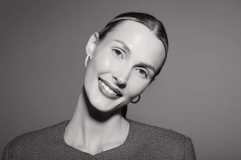 Smiling caucasian woman with light skin and slicked hair posing on gray background in cozy sweater studio portrait.