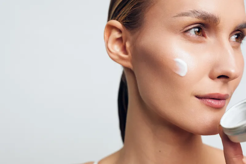 Woman skincare closeup, applying cream on face from cosmetic jar, spa moisturizer texture, calm expression, soft lighting, minimal background, beauty care