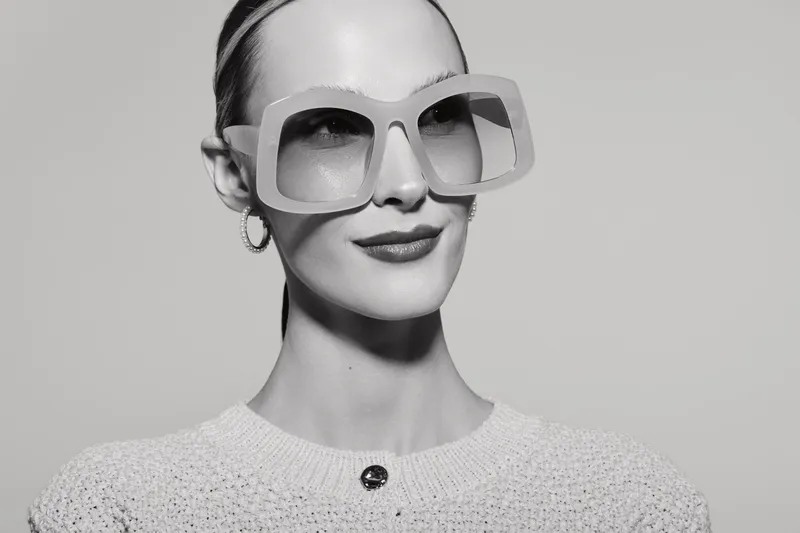 Portrait of a stylish white woman with fair skin wearing oversized sunglasses and hoop earrings on a light background. Fashion and elegance concept.