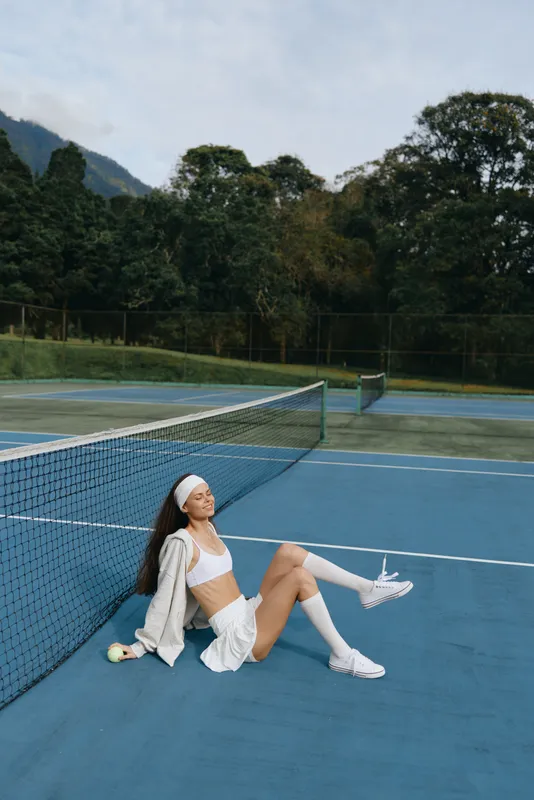 Young female tennis player relaxing on the court, wearing sporty attire and conveying a joyful expression, ideal for sports and wellness themes