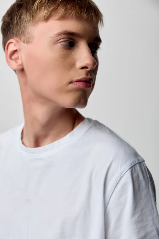 Side profile of a young man in a white tee, thoughtful expression, studio lighting, minimalist background, fashion concept, contemporary mood for stock usage, clean lines, neutral tones, versatile