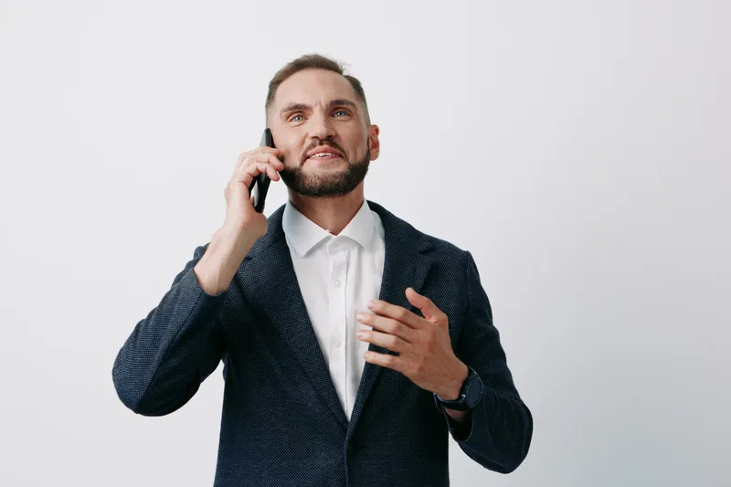 A confident business professional man speaks on a mobile phone, showing engaged emotions and urgency. He stands against an isolated colored background, conveying leadership and focus.