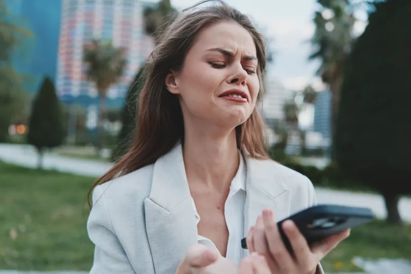 upset woman holding smartphone outdoors frustrated stressed financial crisis emotional portrait
