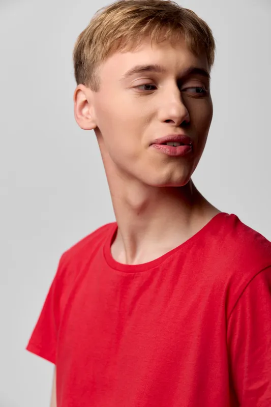 Young male in a red shirt, side profile, thoughtful expression under studio lighting for a casual headshot, suitable for fashion, lifestyle branding and contemporary creative projects
