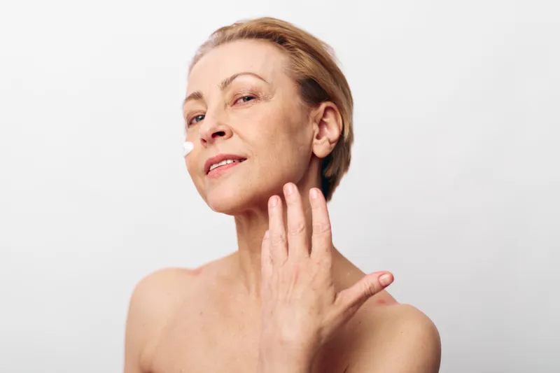 Confident mature woman with short hair gently touching her neck, showcasing natural skin and beauty on a clean white background. Concept of aging gracefully and self-care.