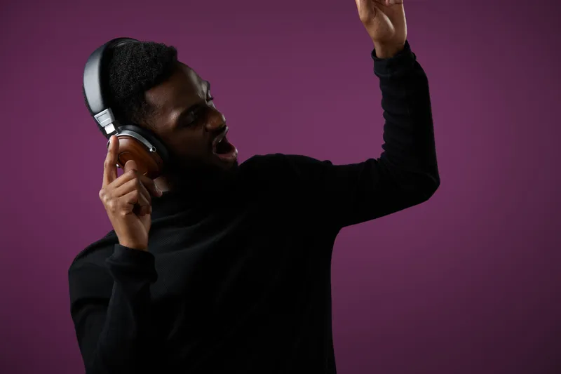 Young African man dancing with headphones, expressing joy and passion against a purple background, showcasing vibrant emotions and modern lifestyle