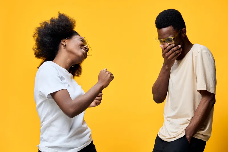 Happy young Afro American couple enjoying music and dancing against a vibrant yellow background, showcasing joy and connection through their expressive emotions
